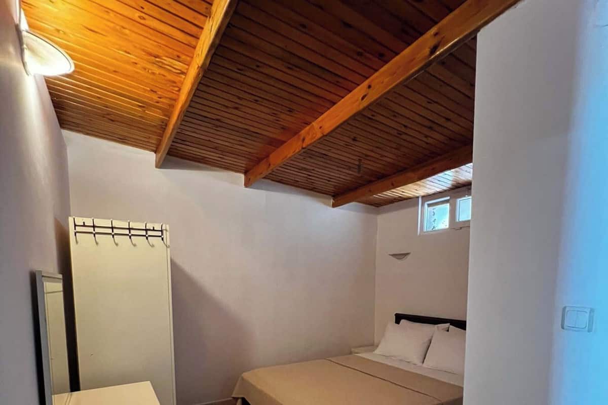 A small, single-room apartment with a sloped ceiling, a bed, a small desk, and a mirror.