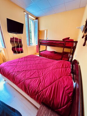 A room with bunk beds, a television, a window with curtains, and a wooden floor. - F1 30M2 2/4 persons (La Bourboule)