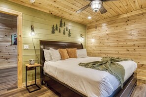 Ein Zimmer mit Holzwänden, einem Bett, einem Nachttisch, einer Wandleuchte und einem Deckenventilator.