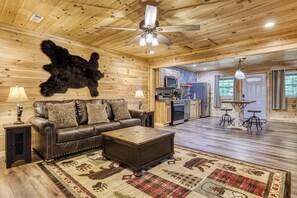 Ein Holzinnenraum mit Ledersofa, Couchtisch, Deckenventilator und Küchenzeile.