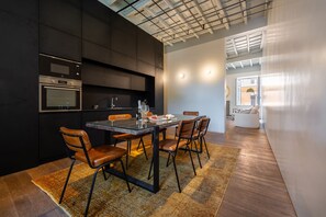 Eine moderne Küche mit integrierten Geräten, ein Essbereich mit Glastisch und Ledersesseln sowie ein gemütlicher Wohnbereich mit einer Couch und einem großen Fenster.