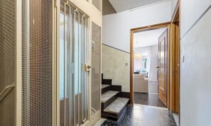 Ein Flur mit einer Treppe, die zu einem Zimmer führt, einer Tür mit Holzrahmen und einem Drahtgitter links.