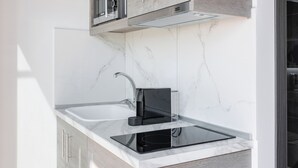 A modern kitchen with a built-in microwave, a black induction cooktop, and a glass backsplash. - Sani Gulf I & II (Kassandra)
