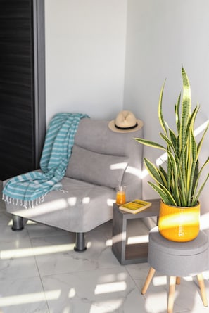 A modern living room with a grey sofa, a striped throw blanket, a small table with a drink, a hat, and a potted plant. - Sani Gulf I & II (Kassandra)
