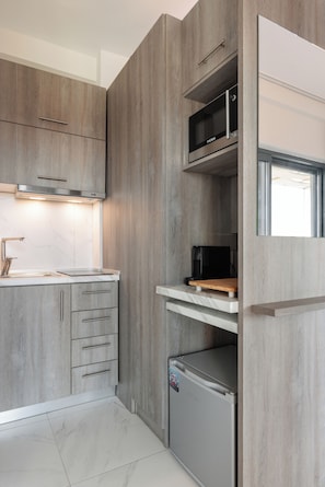 A modern kitchen with wood paneling, a built-in microwave, a coffee maker, and a small refrigerator. - Sani Gulf I & II (Kassandra)