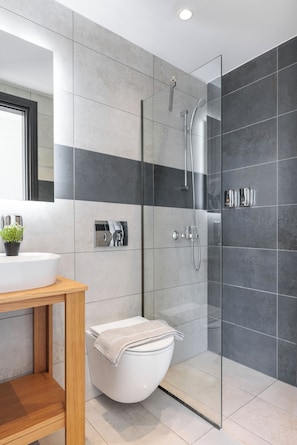 A modern bathroom with a glass-enclosed shower, a white toilet, and a wooden vanity. - Sani Gulf I & II (Kassandra)