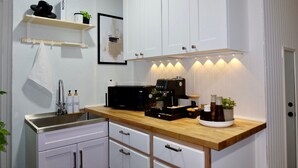 A kitchen with white cabinets, a wooden countertop, a coffee machine, and a sink. - Cozy Private Studio near Ibor & Port (Tampa)