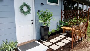 A house with a white door, a wreath, a potted plant, a wooden bench, and a lattice fence. - Cozy Private Studio near Ibor & Port (Tampa)