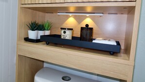 A wooden cabinet with a shelf containing potted plants, a container labeled 'Vanilla Bean,' and a small black tray. - Cozy Private Studio near Ibor & Port (Tampa)