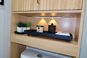 Ein Holzschrank mit einer Ablage, auf der Blumentöpfe, ein Behälter mit der Aufschrift 'Vanilla Bean' und eine kleine schwarze Schale stehen.