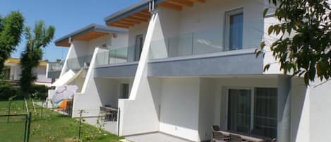 A modern two-story house with a flat roof, large windows, and a patio with outdoor furniture.