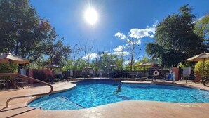 Ein Pool mit gewölbter Kante, umgeben von Liegestühlen und Sonnenschirmen.