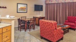 Ein Hotelzimmer mit Essbereich, Fernseher, einem roten Sessel und einer Küchenarbeitsplatte.