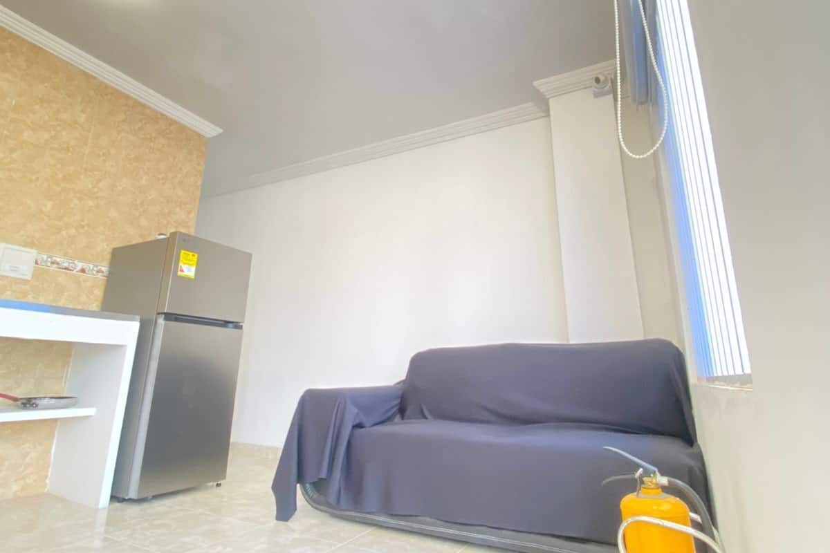 A room with a sofa, a small table, a refrigerator, and a yellow fire extinguisher.