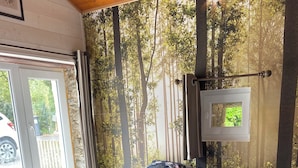Une chambre à coucher avec une couvre-lit à motifs floraux, une vue sur les arbres par la fenêtre et une porte donnant sur l’extérieur.