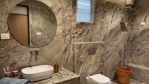 Un baño con pared de mármol, un espejo redondo, un lavabo, un inodoro y una ducha.