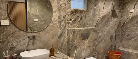 A bathroom with a marble wall, a round mirror, a sink, a toilet, and a shower.