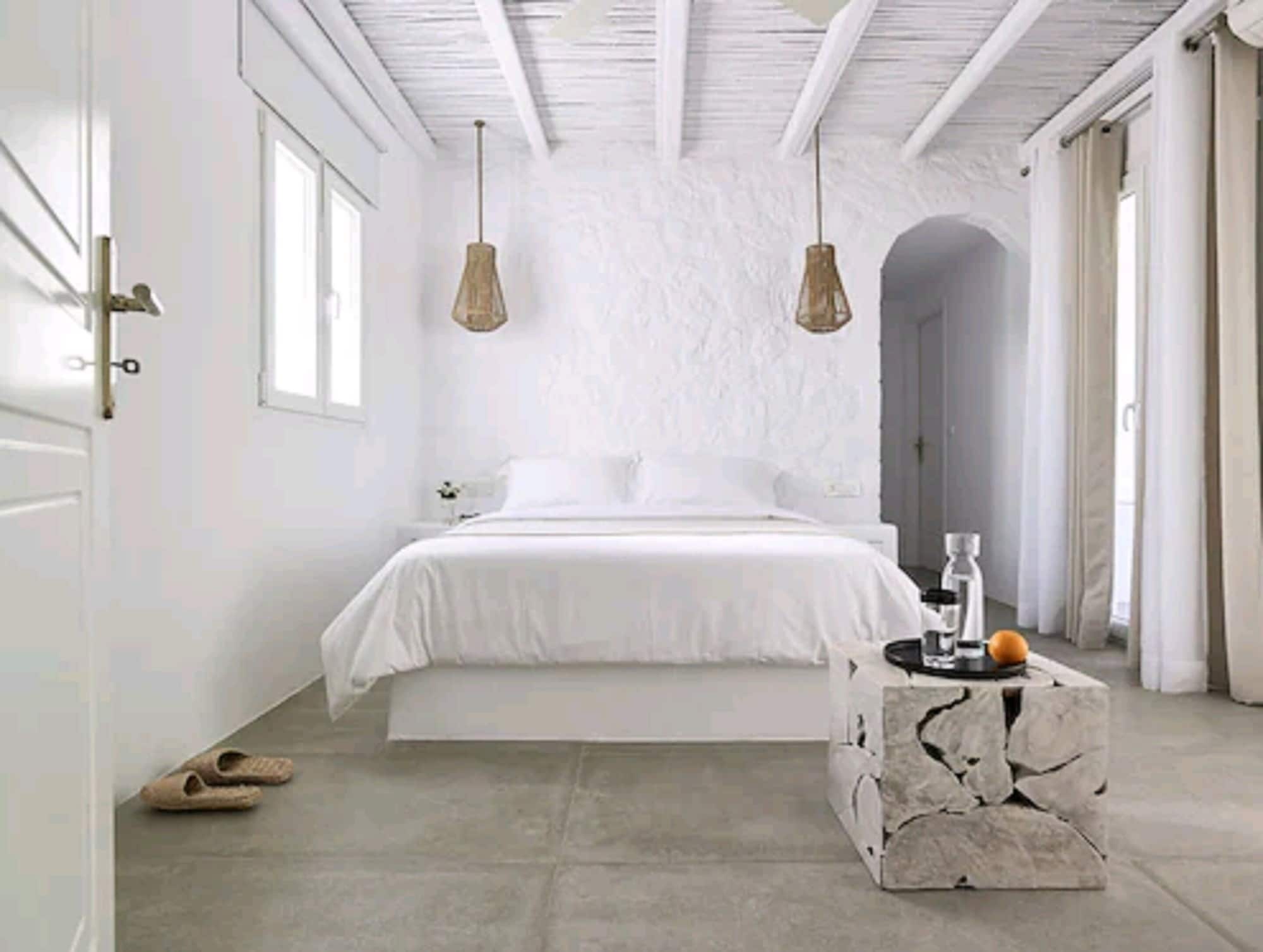 A bedroom with a bed, two pendant lights, a stone coffee table, and a door.