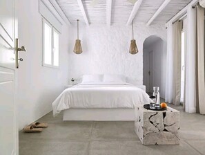 Un dormitorio con una cama, dos lámparas colgantes, una mesa de centro de piedra y una puerta.