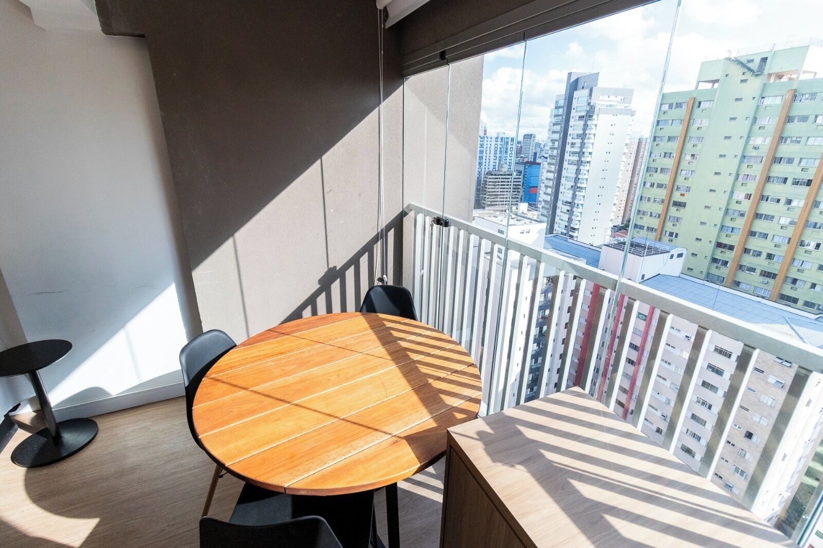 Ein Balkon mit rundem Holztisch und zwei Stühlen mit Blick auf eine Skyline und hohe Gebäude.