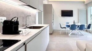 A modern kitchen with a built-in oven, a coffee maker, and a sink. There is a dining area with a table and chairs, and a flat-screen TV mounted on the wall. - Hostdomus - Princess Suite (Marina di Andora)