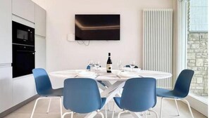 A modern kitchen with built-in appliances, a dining table with chairs, and a mounted TV. - Hostdomus - Princess Suite (Marina di Andora)