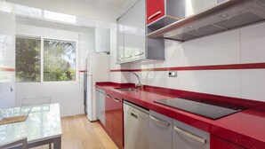 A modern kitchen with stainless steel appliances, a red countertop, and a window with a view of trees. - Apartment 'Ducal Mar' with Shared Garden, Wi-Fi and Air Conditioning (Grau i Platja)