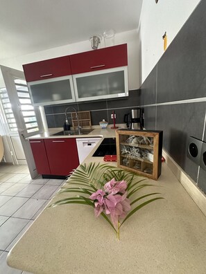 A modern kitchen with red cabinets, a stainless steel coffee maker, and a decorative plant on the counter. - Cosy sweet Home - Villa 4-6 pers - Swimming pool and Quiet area (Sainte-Anne)