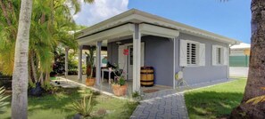 A single-story building with a covered porch, a barrel outside, and a paved walkway. - Cosy sweet Home - Villa 4-6 pers - Swimming pool and Quiet area (Sainte-Anne)