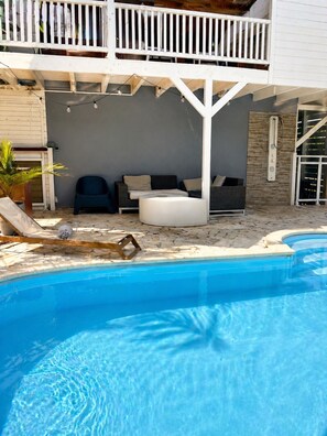 A pool with a white deck, a lounge area with seating, and a covered balcony. - Cosy sweet Home - Villa 4-6 pers - Swimming pool and Quiet area (Sainte-Anne)