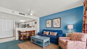A living room with a blue sofa, a patterned armchair, a coffee table, and a rug. - Oceanfront 2BR 2BA, Pools, Hot Tub, Epic Views (Myrtle Beach)