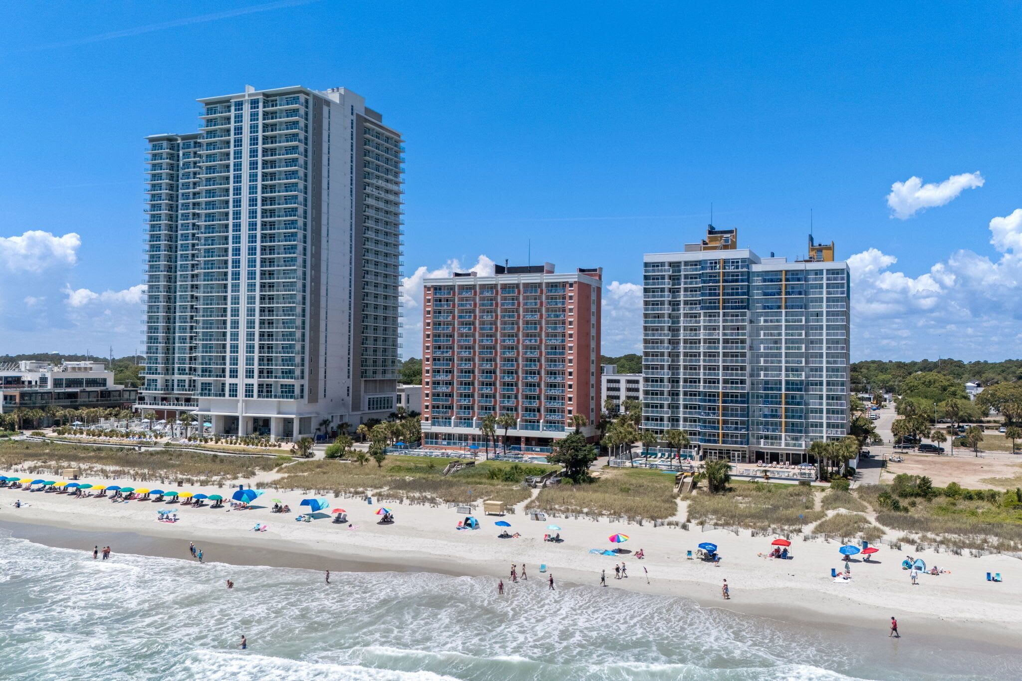 A beachfront hotel with high-rise buildings, a sandy beach, and umbrellas.