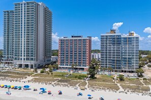 Ein Hotel direkt am Strand mit mehreren Hochhäusern, einem Sandstrand und einem Poolbereich.