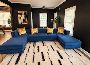 A sectional sofa with gold accent pillows, a patterned rug, and a black and white wall. -     Luxury Atlanta Host Stylish Stays Designed for Comfort & Experience (Atlanta)