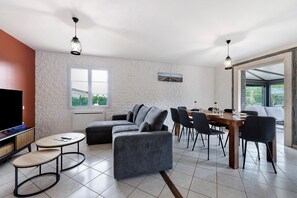 A modern living room with a sectional sofa, a dining table with chairs, and a TV.