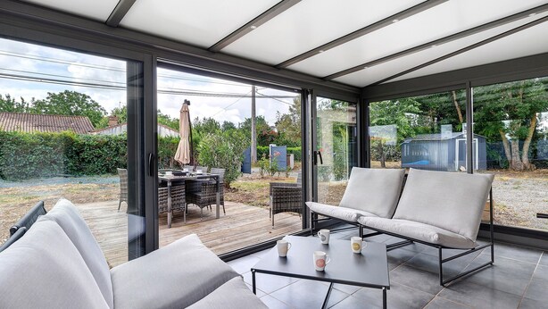 A modern patio with a glass enclosure, outdoor furniture, and a view of the backyard. - Villa Joël – House with Private Pool, 10 Minutes from the Beach (La Jonchère)