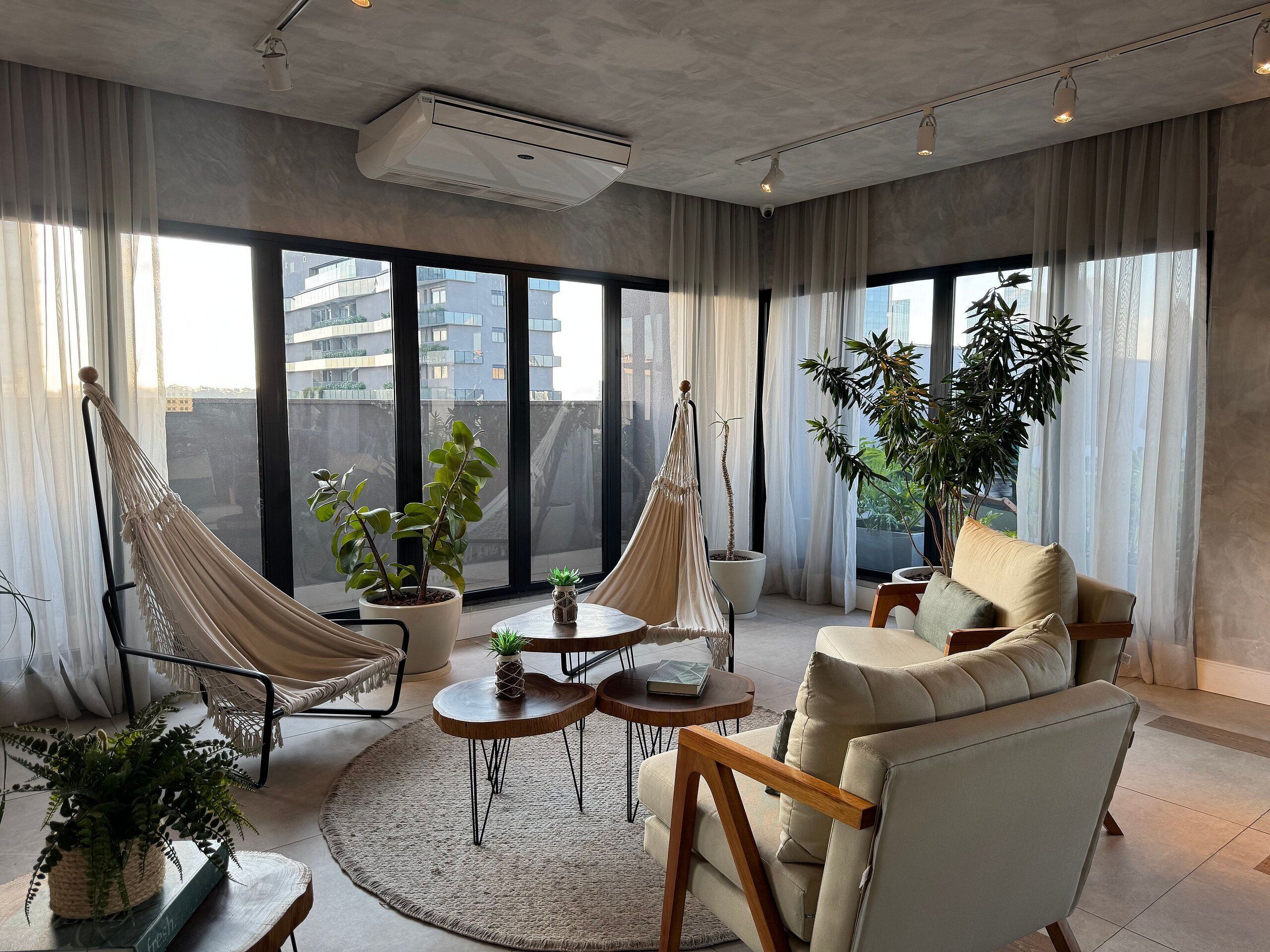 A modern living room with a sofa, two hammocks, a coffee table, and potted plants.