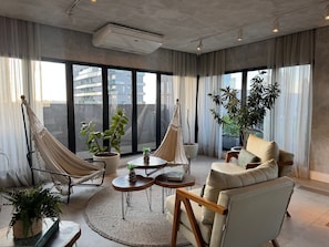 A modern living room with a sofa, two hammocks, a coffee table, and potted plants. - Studio recém-construído no coração da Vila Olímpia (São Paulo)