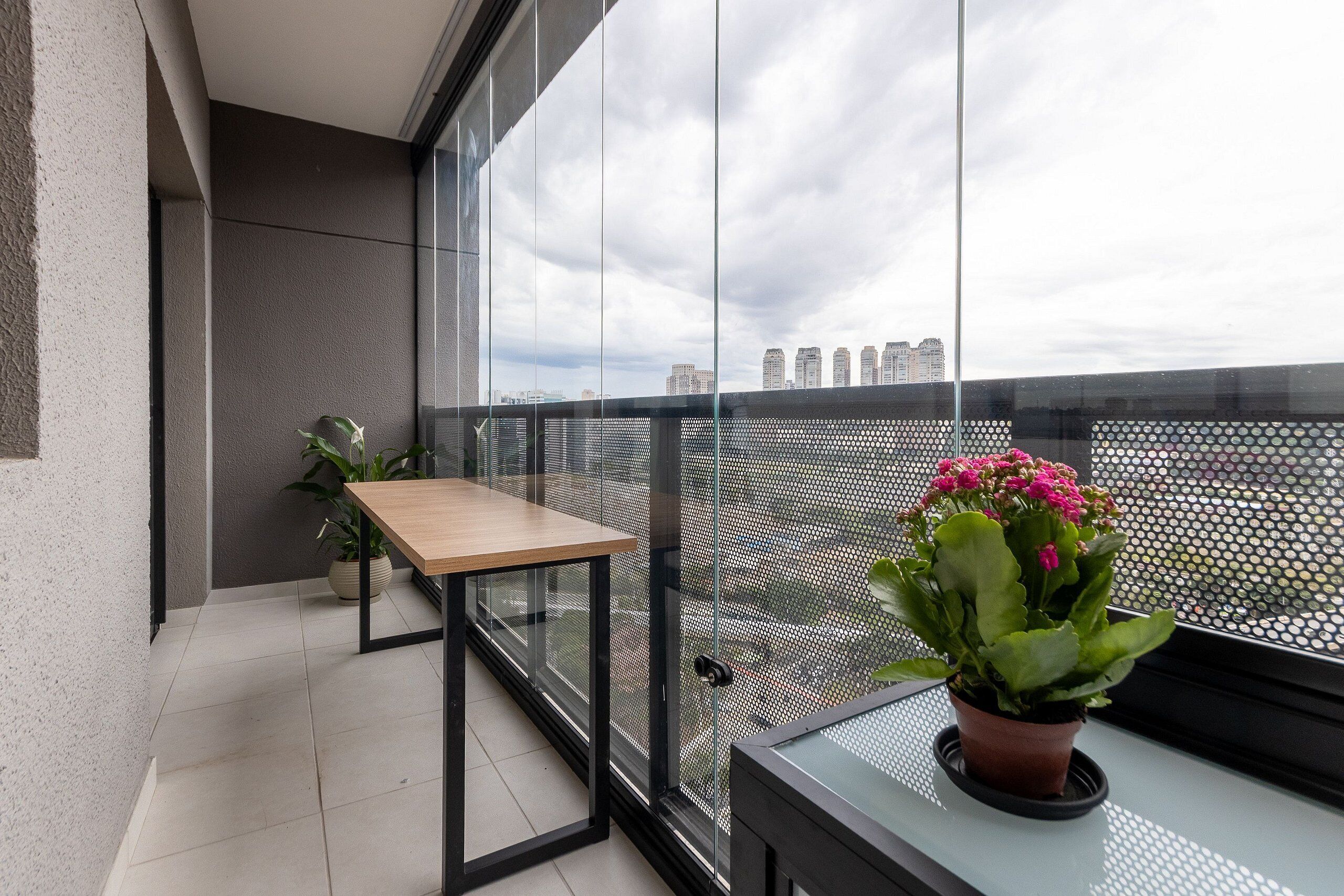 A balcony with a table, potted plants, and a view of the city skyline.