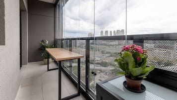 A balcony with a table, potted plants, and a view of the city skyline.
