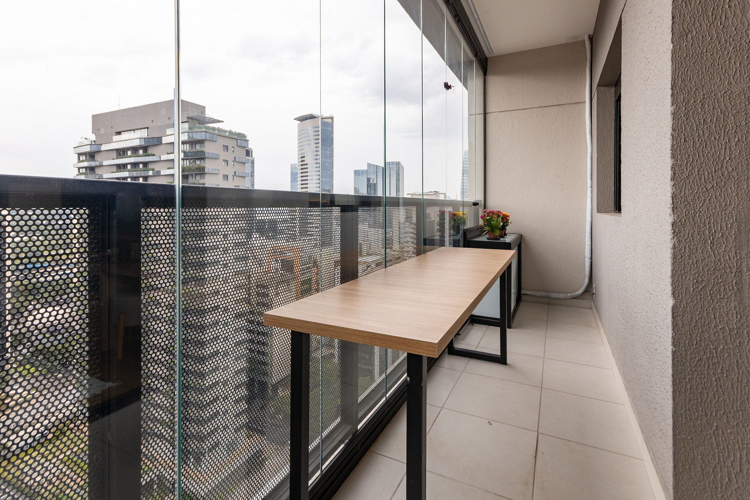 Ein Balkon mit Holztisch, einer kleinen Pflanze und Blick auf Stadtgebäude.