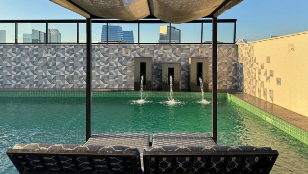 A rooftop pool with geometric patterned walls, a clear sky, and a cityscape view. - Studio recém-construído no coração da Vila Olímpia (São Paulo)