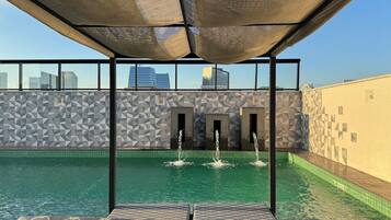 A rooftop pool with geometric patterned walls, a clear sky, and a cityscape view.