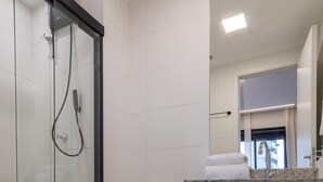 A bathroom with a glass-enclosed shower, a toilet, and a wooden vanity with a sink. - Studio recém-construído no coração da Vila Olímpia (São Paulo)