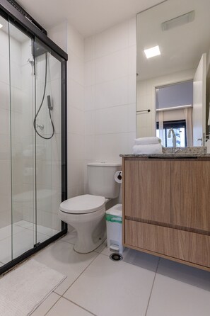 Kylpyhuoneessa on lasiseinällä varustettu suihku, wc ja puinen allaskaappi, jossa on pesuallas.