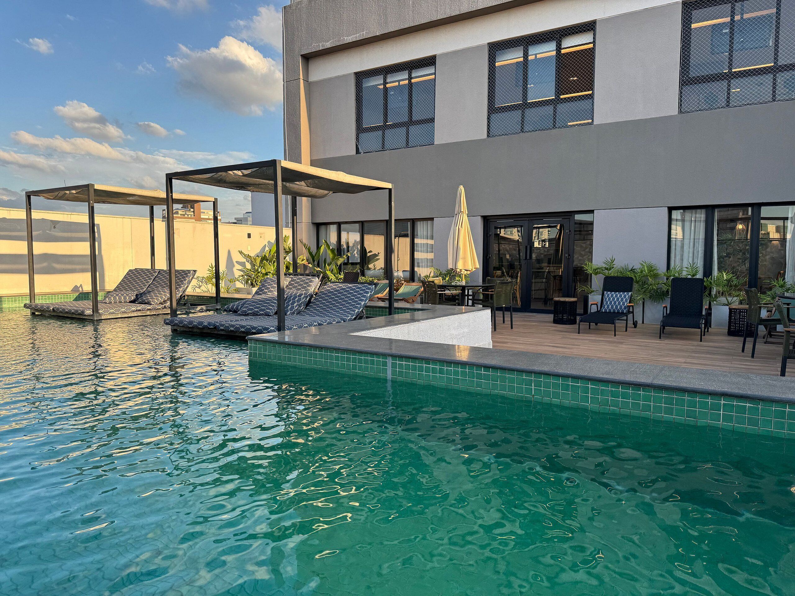A modern building with a swimming pool, outdoor seating, and a covered area with lounge chairs.