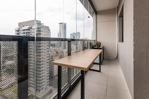 A balcony with a wooden table, a small plant, and a view of city buildings. - Studio recém-construído no coração da Vila Olímpia (São Paulo)