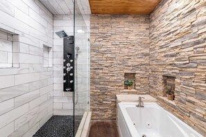 A modern bathroom with a glass shower, a stone wall, and a white bathtub. - Pottsboro Lodge - Sleeps 15 - Hot Tub & Patio (Pottsboro)