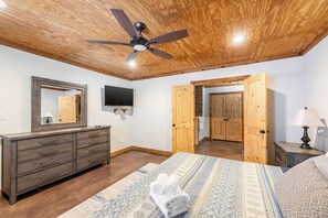 A bedroom with a bed, a dresser, a ceiling fan, a TV, and wooden doors. - Pottsboro Lodge - Sleeps 15 - Hot Tub & Patio (Pottsboro)