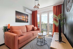 A modern living room with a sofa, a small table, a potted plant, and a cityscape painting. - Modern Apartments with Balconies | Downtown (Gdańsk)